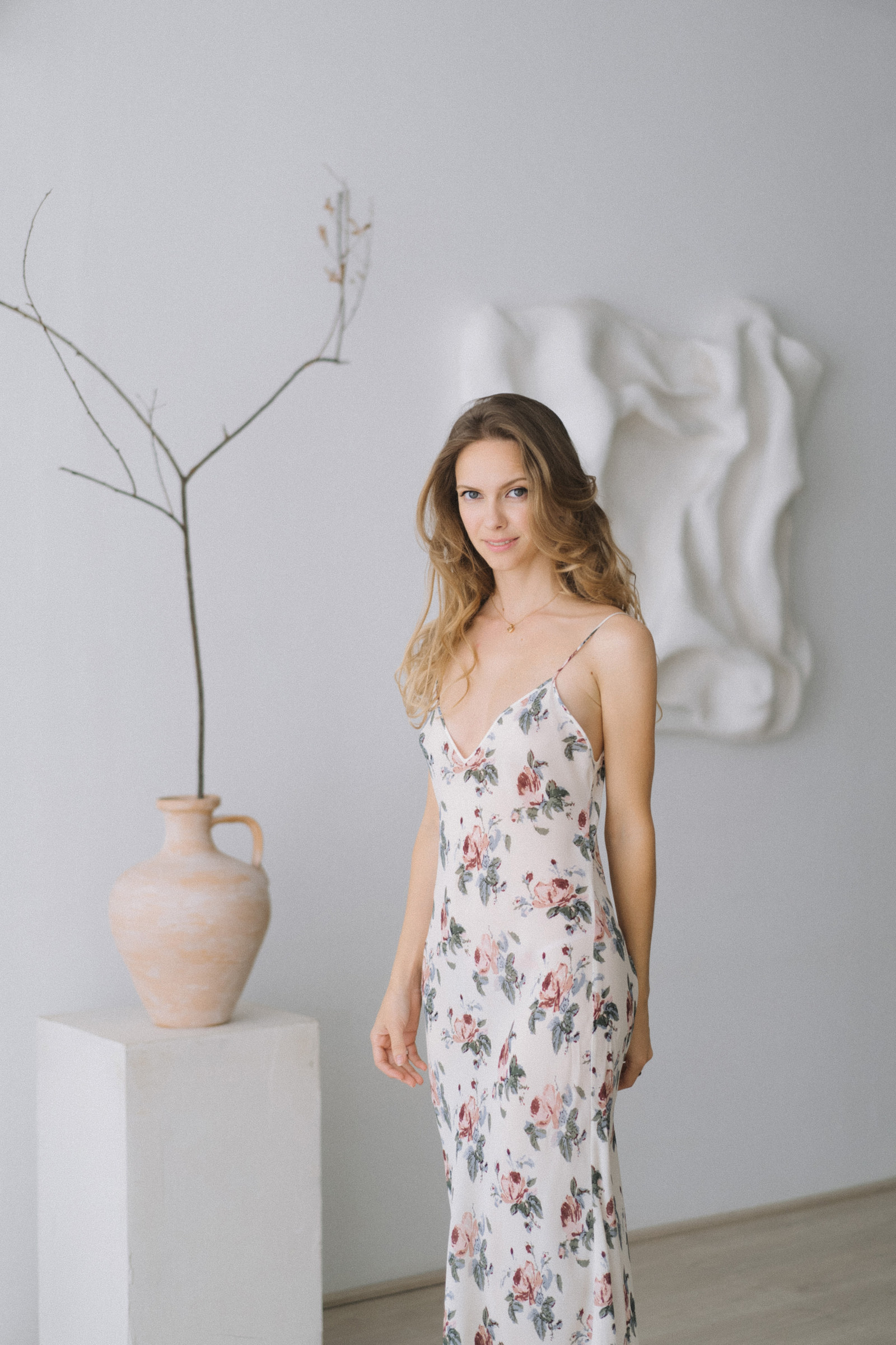 Nata in a floral slip dress in a white room, beside a clay vase