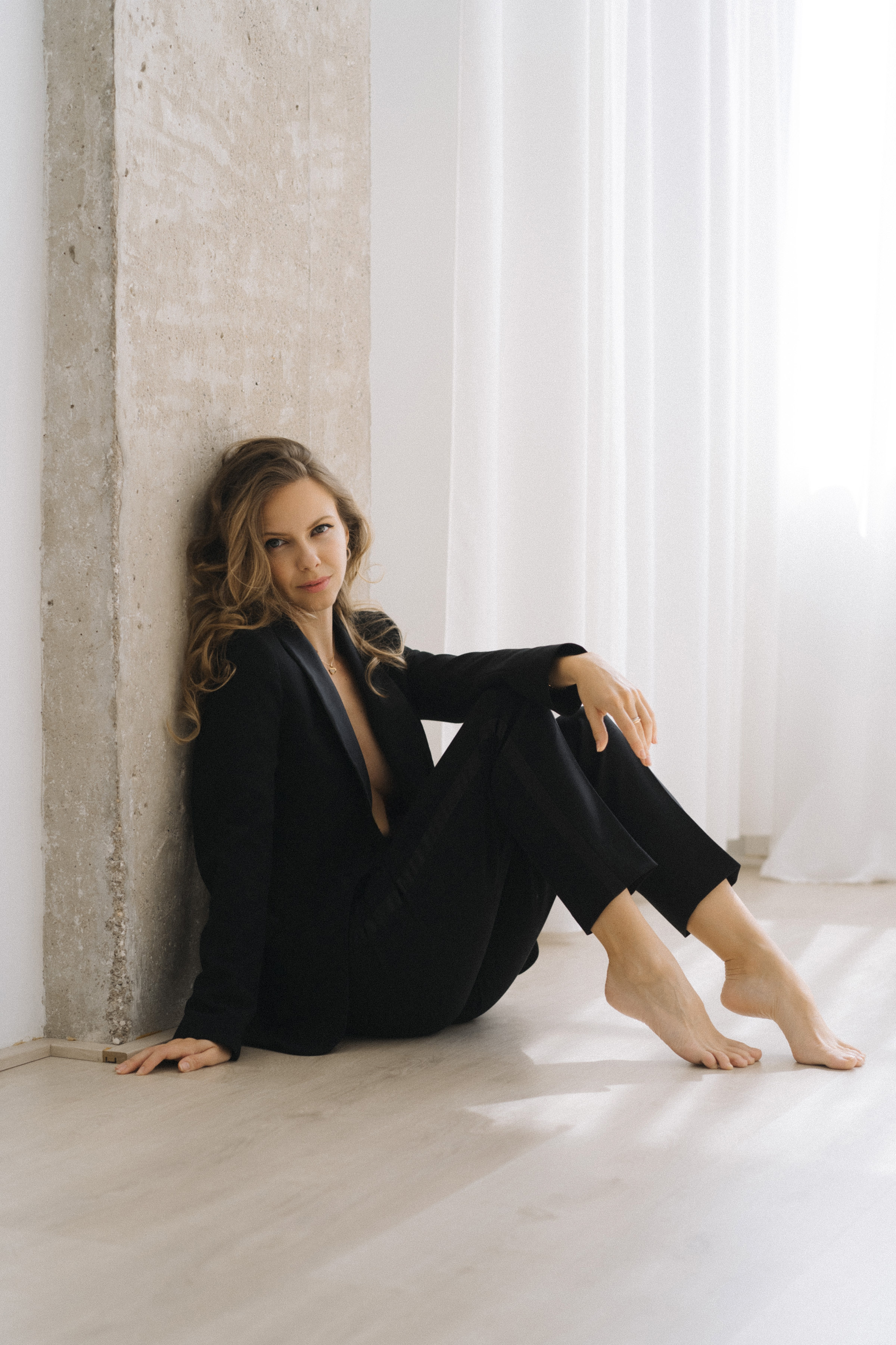 Nata Lomadze in a black suit, sitting on the floor by a concrete pillar in soft daylight